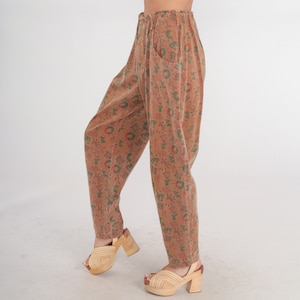 K&ouml;nnte beinhalten: Hoch taillierte Hose in einem gedeckten Braunton mit einem durchgehenden geometrischen und sonnenf&ouml;rmigen Druck in Gr&uuml;n- und Rott&ouml;nen. Die Hose hat eine lockere Passform, einen gerafften elastischen Bund und seitliche Eingrifftaschen.