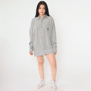 May include: A gray oversized button-down shirt with a small embroidered design on the left chest pocket.
