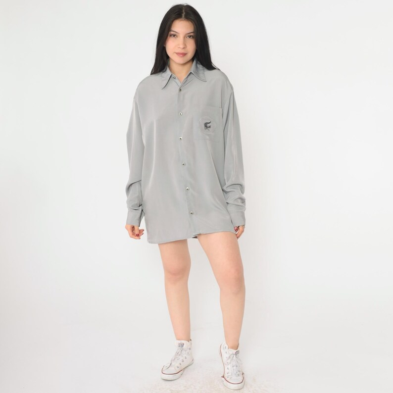 May include: A gray oversized button-down shirt with a small embroidered design on the left chest pocket.