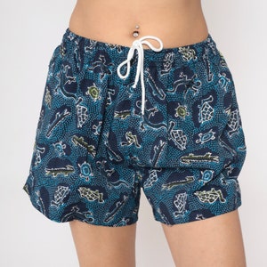 May include: Blue and green patterned shorts with a drawstring waist. The pattern features small animals and dots.