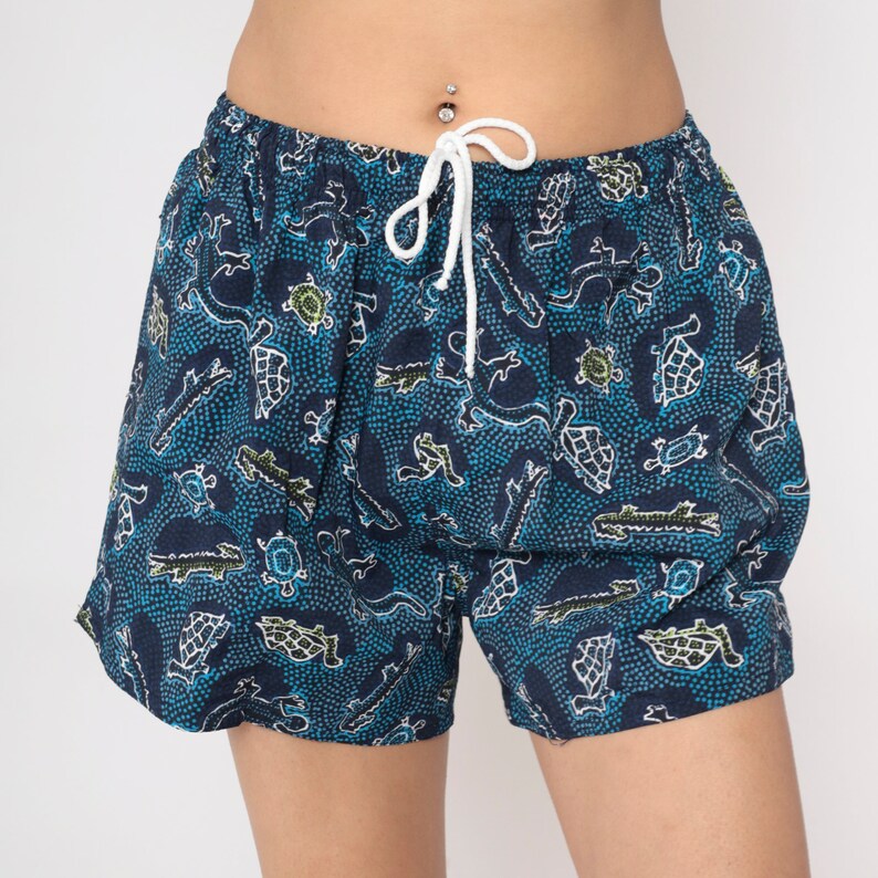 May include: Blue and green patterned shorts with a drawstring waist. The pattern features small animals and dots.