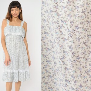 May include: A white dress with a blue floral print and a lace trim. The dress has a sleeveless design and a ruffled neckline.
