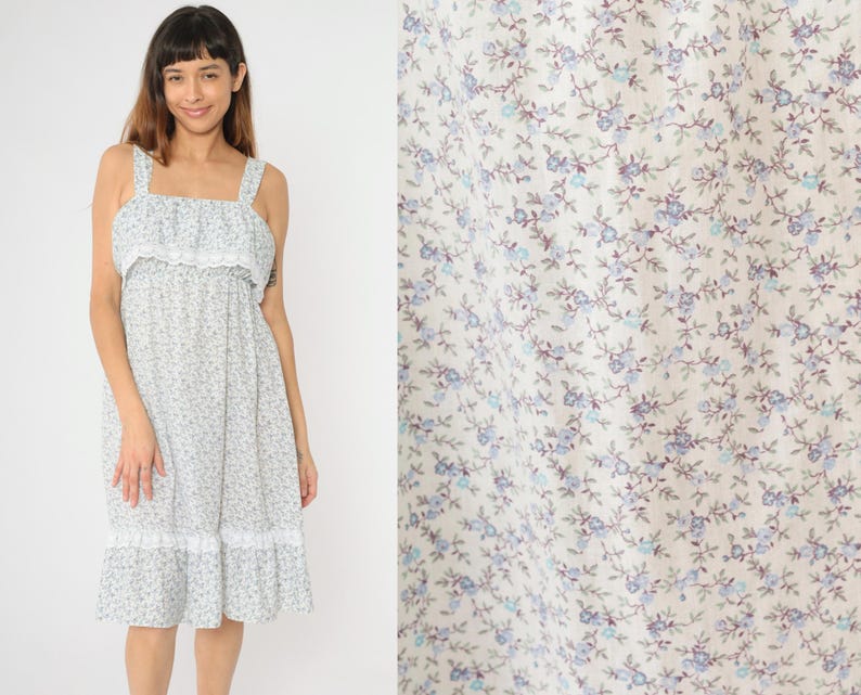 May include: A white dress with a blue floral print and a lace trim. The dress has a sleeveless design and a ruffled neckline.