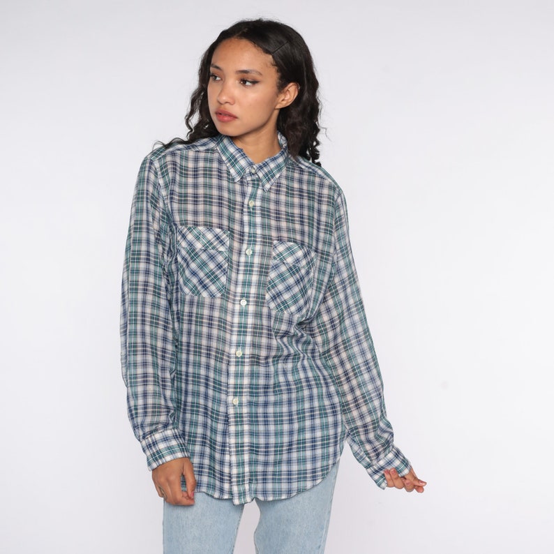 Op de afbeelding: Een geruit shirt met lange mouwen in tinten blauw, groen en wit. De blouse heeft twee borstzakken en een knoopsluiting. Het model draagt het shirt met een lichtblauwe jeans.