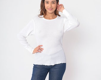 May include: A white long-sleeved thermal shirt with a ribbed texture. The shirt has a crew neckline and a relaxed fit.