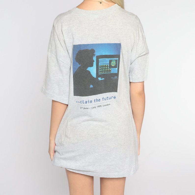 May include: Gray t-shirt with a graphic print of a person sitting in front of a computer screen. The text "...claim the future" and "27 June - 1 July 1999, London" is printed below the graphic.