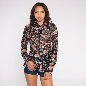 Op de afbeelding: Zwart overhemd met bloemenpatroon in roze, oranje en paarse tinten. Het shirt met lange mouwen heeft een klassieke kraag en manchetten met knopen. Het bloemmotief staat tegen een zwarte achtergrond.