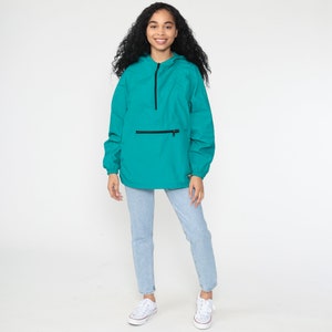 May include: A teal blue hooded jacket with a black zipper and a black zippered pocket on the front. The jacket is made of a lightweight material and has a relaxed fit.