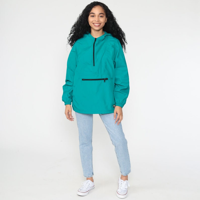 May include: A teal blue hooded jacket with a black zipper and a black zippered pocket on the front. The jacket is made of a lightweight material and has a relaxed fit.