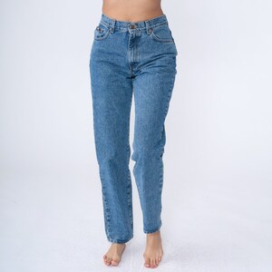 May include: Light blue denim jeans with a classic five-pocket design. The jeans have a straight leg cut and a button and zip closure. The denim has a medium wash and a slight fade. The jeans are a casual style.
