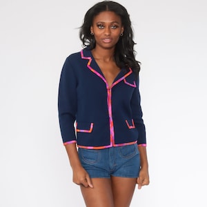 May include: A navy blue cardigan with a pink and orange floral trim. The cardigan has a collar, long sleeves, and two pockets.