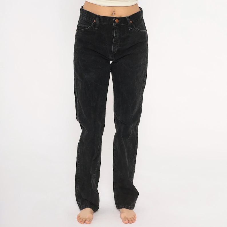 May include: Black denim jeans with a classic five-pocket design. The jeans have a button and zip closure and a straight leg fit. The dark wash denim has a slightly faded appearance. The jeans are worn by a person.
