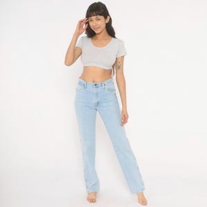Op de afbeelding: Een lichtgrijs, kort mouw crop top en lichtblauwe jeans. De jeans hebben een klassieke, rechte pijp. Het model staat voor een witte achtergrond.