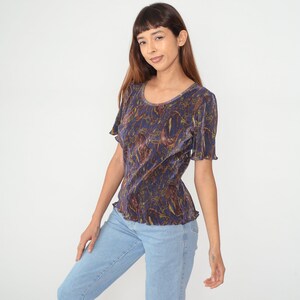 Puede incluir: Una blusa de color morado y dorado con estampado floral y un dobladillo con volantes. La blusa est&aacute; hecha de una tela suave y sedosa.