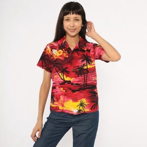 Könnte beinhalten: Ein rotes Kurzarmhemd mit tropischem Landschaftsdesign mit Palmen, Sonnenuntergang und floralen Akzenten. Das Hemd hat eine Knopfleiste und einen Kragen. Das Hemd wird mit einer blauen Jeans kombiniert.