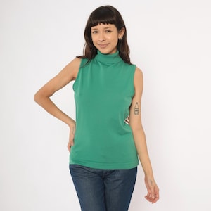May include: A sleeveless, emerald green turtleneck top. The top is made of a soft, knit fabric and has a ribbed hem. The model is wearing blue jeans. The top is a vintage style.