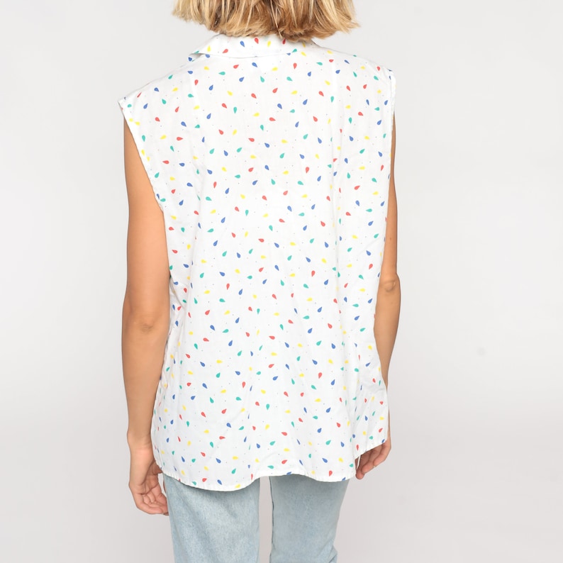 May include: White sleeveless top with a colorful teardrop pattern in red, yellow, blue, and green. The top has a collared neckline and a relaxed fit. The fabric appears to be lightweight and suitable for warm weather.