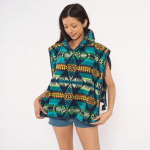 May include: A hooded poncho featuring a vibrant geometric pattern in shades of navy blue, teal, lime green, yellow, and orange. The garment is constructed from a soft fleece material and includes a hood, wide arm openings, and dark blue trim.