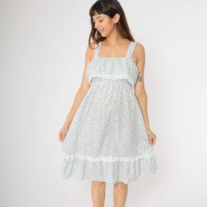 May include: A white dress with a floral print and lace trim. The dress has a square neckline and thin straps.