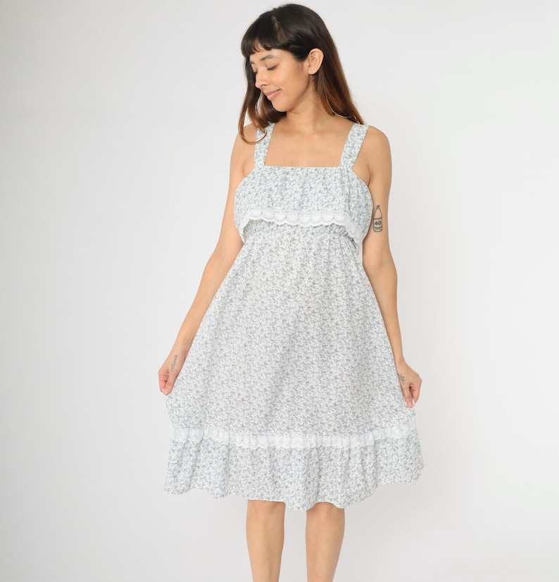 May include: A white dress with a floral print and lace trim. The dress has a square neckline and thin straps.