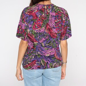 May include: A purple, pink, green, and red short-sleeved shirt with a floral print.