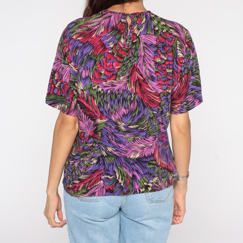 May include: A purple, pink, green, and red short-sleeved shirt with a floral print.