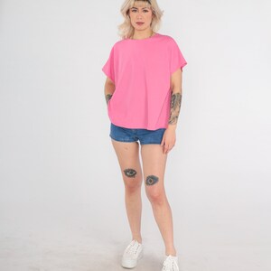 May include: A pink short-sleeved shirt with a ribbed texture. The model is wearing denim shorts and white sneakers.