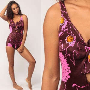 May include: A vintage one-piece swimsuit in a brown floral print with pink and orange accents. The swimsuit features a bow detail at the bust and a keyhole cutout. The fabric has a shiny appearance.