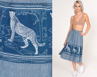 May include: Blue denim skirt featuring a white cheetah print border. The skirt has an elastic waistband and a mid-calf length. The cheetah design is repeated around the hemline, creating a unique and eye-catching pattern.