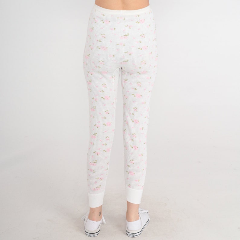 May include: White thermal underwear with a pink floral pattern. The underwear has a ribbed texture and a fitted silhouette.