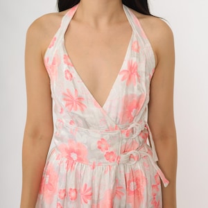 May include: A halter-neck dress with a floral pattern in shades of pink and white. The dress features a V-neckline and a wrap-style design with a tie closure at the waist. The fabric has a subtle sheen, and the overall style is feminine and summery.
