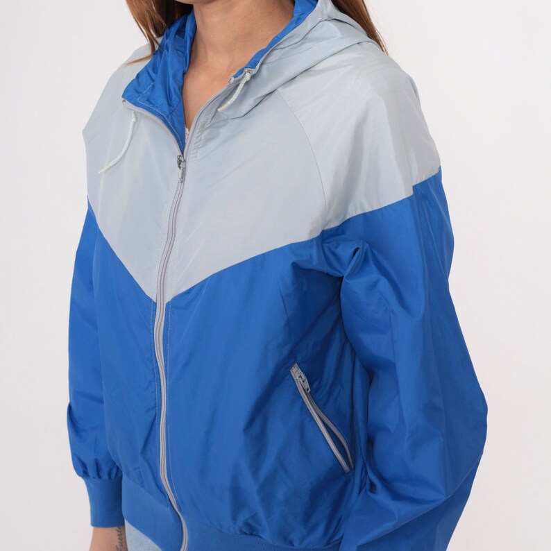 May include: A blue and gray hooded jacket with a zipper closure. The jacket has a contrasting color design with a gray hood and a blue body.