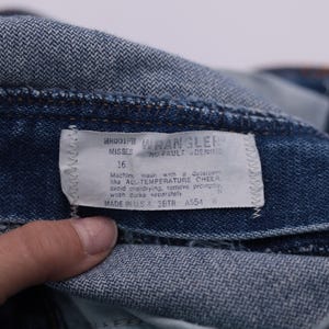 May include: Close-up of a blue denim Wrangler jeans label with the text "ROOP WRANGLER MISSES 16 WO-PAULT DENIM" and care instructions. Machine wash with All-Temperature Cheer, avoid overdrying, remove promptly, wash dark separately. Made in USA SBTR A554.