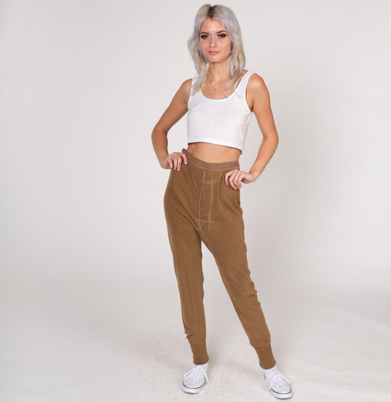 Op de afbeelding: Een vrouw draagt een wit tanktop en een bruine broek. De broek heeft een trekkoord in de taille en een ontspannen pasvorm.