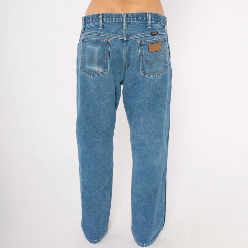 Puede incluir: Vaqueros de mezclilla azul claro con un dise&ntilde;o cl&aacute;sico de cinco bolsillos. Los vaqueros presentan un parche de cuero marr&oacute;n en el bolsillo trasero y el logotipo de Wrangler. Los vaqueros tienen un corte de pierna recta y est&aacute;n hechos de un material de mezclilla duradero.