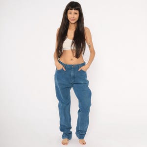 May include: A person wearing a white crop top and blue jeans. The jeans are a medium wash denim with a relaxed fit. The person is standing in front of a white background.