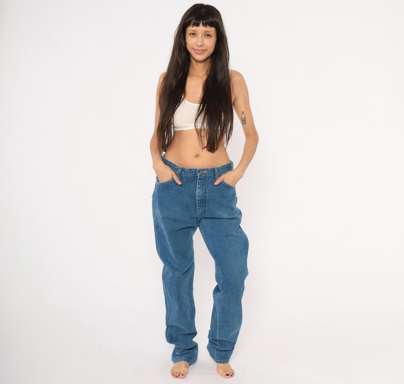 May include: A person wearing a white crop top and blue jeans. The jeans are a medium wash denim with a relaxed fit. The person is standing in front of a white background.