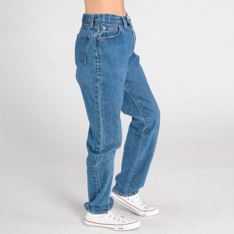 May include: A pair of blue denim jeans with a straight leg fit. The jeans have a high waist and are worn with white trainers.