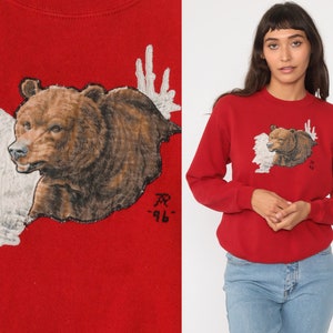 May include: Red sweatshirt with a brown bear and white antlers graphic. The bear is facing left and the antlers are behind it. The text "AR -96" is printed below the bear.