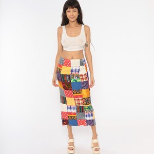 Puede incluir: Una camiseta sin mangas blanca combinada con una falda hasta la pantorrilla con un diseño de patchwork multicolor. La falda está compuesta por varios cuadrados de tela en tonos rojo, azul, amarillo y blanco, con patrones como lunares y cuadros.