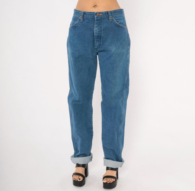 May include: Blue denim jeans with a classic straight leg fit. The jeans have a button and zipper closure, front and back pockets, and are cuffed at the ankles. The model is wearing black platform sandals.