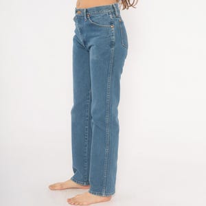 May include: Light blue denim jeans with a classic straight-leg fit. The jeans feature a traditional five-pocket design, a button and zipper closure, and copper-colored rivets. The denim has a medium wash and a slight fade, giving them a vintage look.
