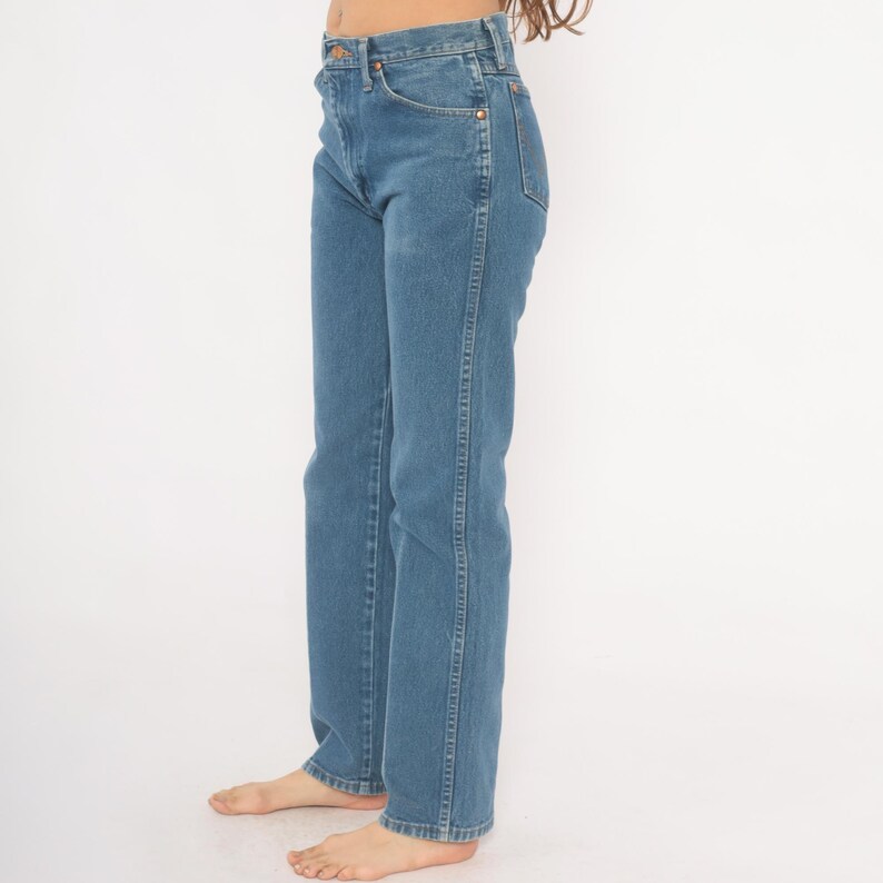 May include: Light blue denim jeans with a classic straight-leg fit. The jeans feature a traditional five-pocket design, a button and zipper closure, and copper-colored rivets. The denim has a medium wash and a slight fade, giving them a vintage look.