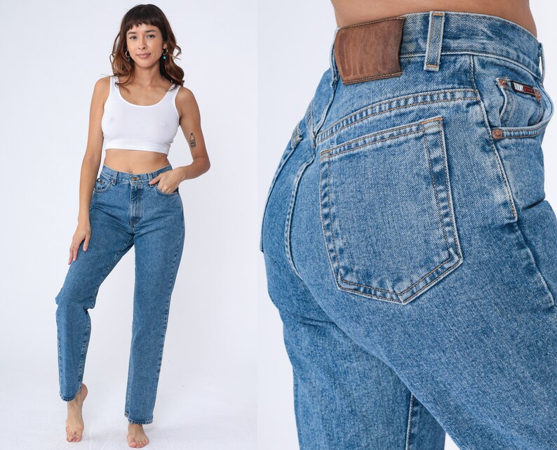 May include: Light blue denim jeans with a classic straight-leg fit. The jeans feature a high waist, front pockets, and a brown leather patch on the back. The model is wearing a white vest top. The jeans are made of a durable denim material.