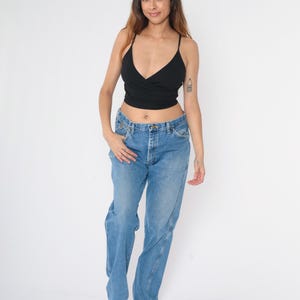 Pu&ograve; includere: Una donna indossa un top corto nero e jeans di denim blu chiaro. I jeans hanno una vestibilit&agrave; rilassata e una gamba dritta.