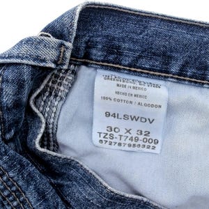 May include: Close-up of blue denim jeans with a white tag. The tag reads "MADE IN MEXICO" and "100% COTTON / ALGODON". The jeans are size 30 x 32.
