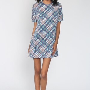 Puede incluir: Un vestido de manga corta con estampado geom&eacute;trico azul, blanco y turquesa. El vestido tiene un escote redondo y un corte holgado.