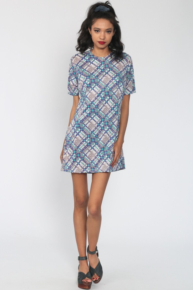 Puede incluir: Un vestido de manga corta con estampado geom&eacute;trico azul, blanco y turquesa. El vestido tiene un escote redondo y un corte holgado.