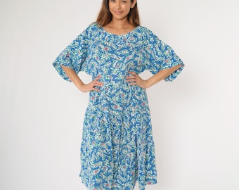 Op de afbeelding: Een blauwe midi-jurk met een witte en groene abstracte print. De jurk heeft een losse pasvorm en korte mouwen.