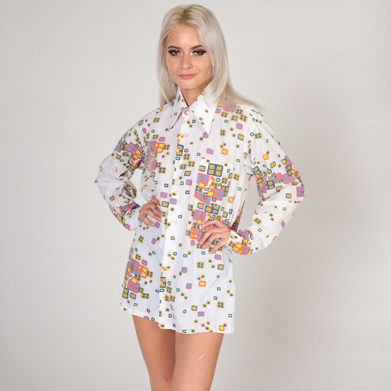 May include: A white long-sleeved shirt with a geometric pattern in shades of blue, pink, yellow, and green. The shirt has a large collar and a button-up front.